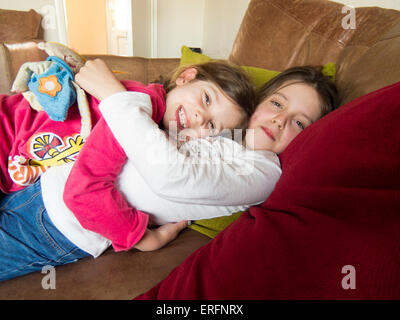 Young sisters hugging on the sofa at home. Stock Photo