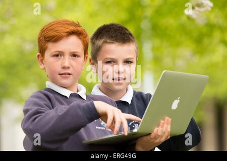 School children learning about technology and computers while outside using laptops. Stock Photo