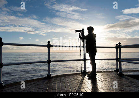 A keen amateur photographer at Penarth Pier in Cardiff taking a picture out to sea while using a monopod for camera support. Stock Photo