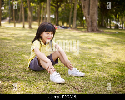 little asian girl sits on grass in park. Stock Photo