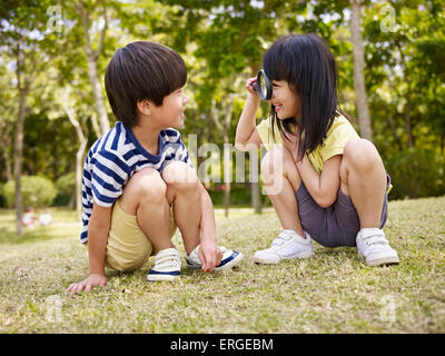 little asian girl looking at little asian boy through a magnifier outdoors in a park. Stock Photo
