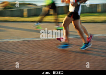 Muscular legs and feet of athletic adult men and woman runners taking early morning exercise on beachfront Stock Photo