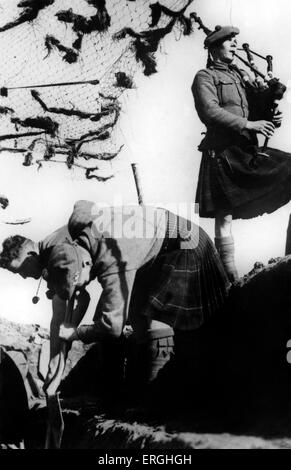 World War 2: Highlanders begin digging a trench, accompanised by a bagpiper. Caption: A detatchment of a Highland Regiment dig Stock Photo