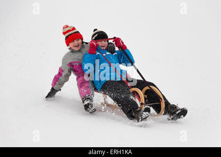 Two little girl in winter activity, sledging on wooden sledge downhill. Concept of winter activity enjoyed by children. Stock Photo