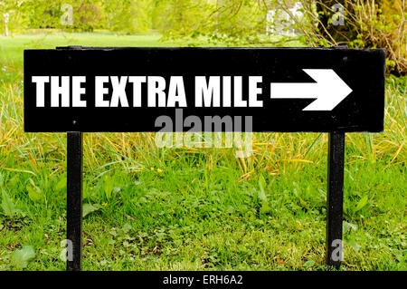 THE EXTRA MILE written on directional black metal sign with arrow pointing to the right against natural green background. Concept image with available copy space Stock Photo