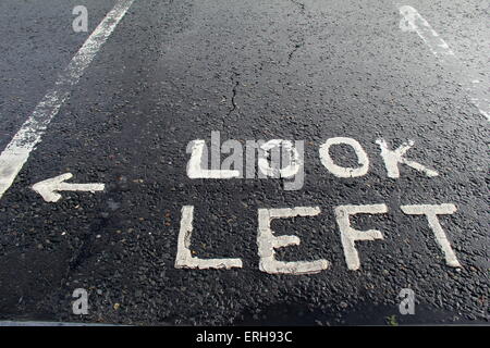 Cracked concrete of parking lot that has sign stating 'look left' painted in bright white on surface Stock Photo