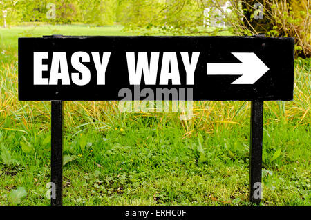 EASY WAY  written on directional black metal sign with arrow pointing to the right against natural green  background. Stock Photo