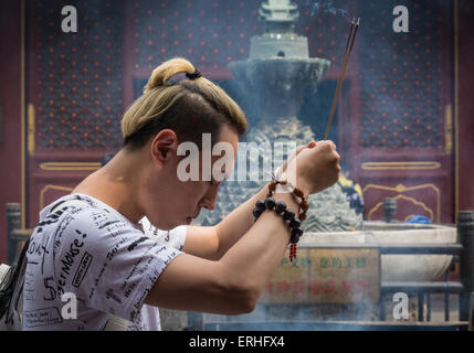 Young Chinese man burning incense while praying at the Lama Temple in Beijing, China Stock Photo