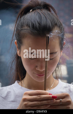 Young Chinese woman burning incense while praying at the Lama Temple in Beijing, China Stock Photo