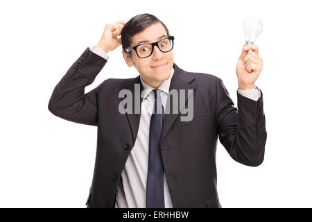 Confused young businessman in a black suit holding a light bulb and scratching his head isolated on white background Stock Photo