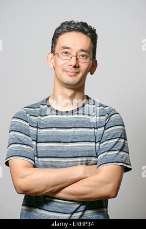 Young male standing with folded hands against gray wall Stock Photo
