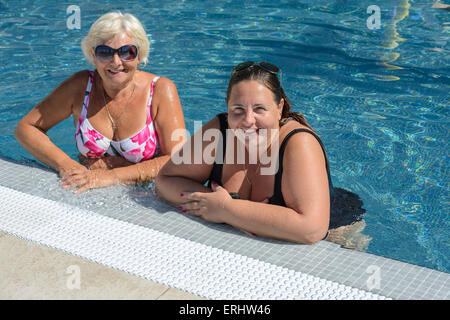 Two tanned smiling women, senior blonde mother and mid adult brunette daughter are standing in bright blue water at the edge of Stock Photo