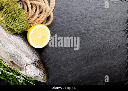 Fresh raw rainbow trout fish with spices on black stone with copy space. Toned Stock Photo