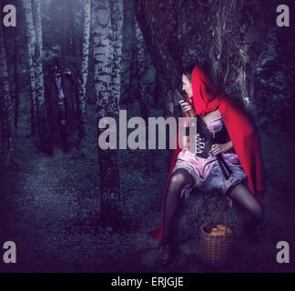 Little Girl Red Riding Hood with automatic in wood sit in ambush behind a tree Stock Photo