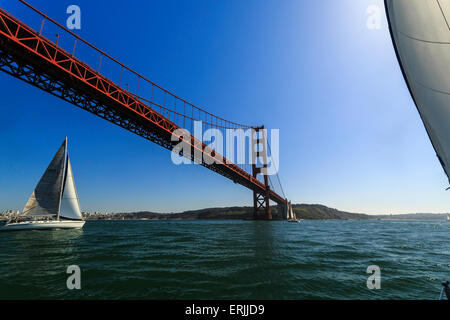 Sailboat passing under the bright red superstructure of the Golden Gate Bridge on a sunny day Stock Photo