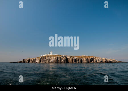 A view of the sea cliffs and lighthouse of Inner Farne from a boat at sea, Farne Islands, Northumberland. June. Stock Photo