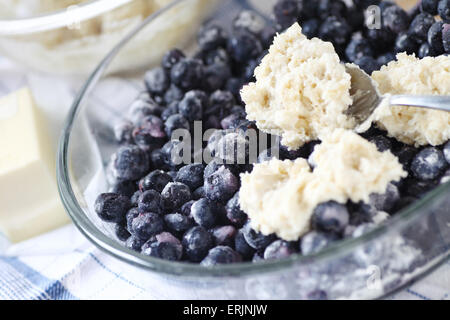 Spooning biscuit dough onto a bowl of sugared blueberries Stock Photo