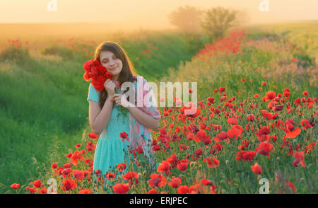 Girl stands in poppy field at sunset Stock Photo