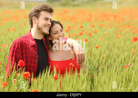 Couple hugging and walking in a green field with red flowers and watching forward Stock Photo