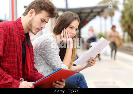 Two students studying concentrated while they are waiting transport in a train station Stock Photo
