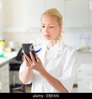 Portrait of an attractive, young, confident female health care professional in his working environment making notes on her smart Stock Photo