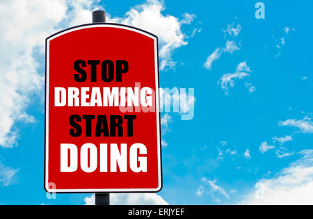 Stop Dreaming Start Doing motivational quote written on red road sign isolated over clear blue sky background. Concept image with available copy space Stock Photo