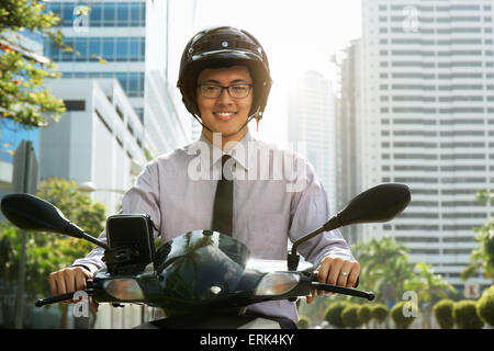 Young asian businessman commuting to job. The man rides a motorcycle scooter with white helmet and smiles at camera Stock Photo