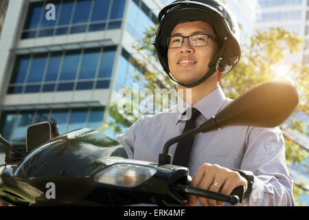Young asian businessman commuting to job in the morning. The man rides a motorcycle scooter with white helmet and looks away Stock Photo