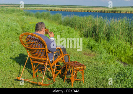 Senior man having rest on a riverside Stock Photo
