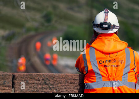 Orion Group Rail Division contractors in Tebay, Cumbria, UK June, 2015. Health and Safety observer for Men at Work. Network Rail Engineers on Settle Carlisle Line, working on rail track maintenance, rail engineer.  Inspectors, Safety engineers, employees, rail workers, workmen, renewing railway lines and Infrastructure surveyors inspecting & measuring the transport freight line track at the summit of Ais Gill. The railway's summit at 1,169 feet (356 metres) is north of Garsdale is the highest mainline in England,  and carries heavily loaded main line freight trains. Stock Photo