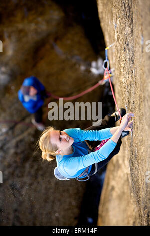 Woman climbing a small crack above her belay partner and a river in Yosemite National Park, California. Stock Photo