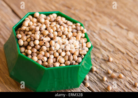 coriander seeds in green bowl on rustic wooden background Stock Photo