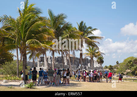 Tourists on a guided tour of the walled Mayan city of Tulum, standing in the shade of palm trees on a hot day, Yucatan, Mexico Stock Photo