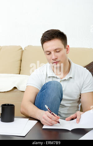 College student concentrating on studying sitting on living room floor with books and notes and pen. Home living lifestyle,  lea Stock Photo