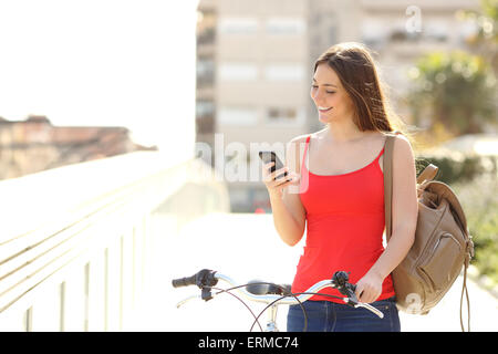 Happy woman using a smart phone walking with a bicycle in an urban park Stock Photo