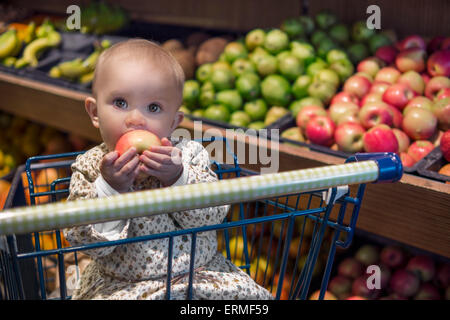 Cute baby in a shopping cart eating an apple Stock Photo