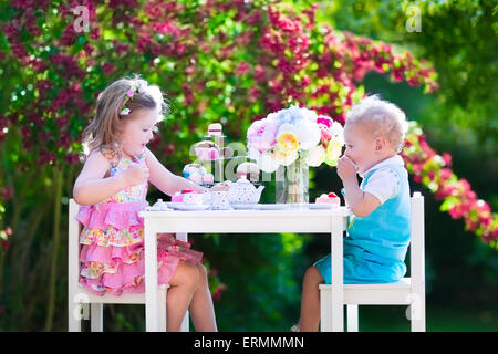Tea garden party for kids. Child birthday celebration. Little boy and girl play outdoor drinking hot chocolate and eating cake. Stock Photo
