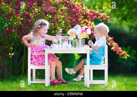 Tea garden party for kids. Child birthday celebration. Little boy and girl play outdoor drinking hot chocolate and eating cake. Stock Photo
