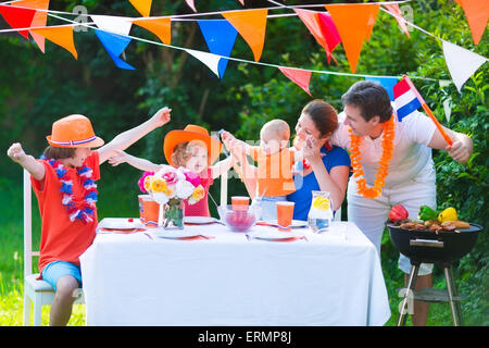 Big Dutch family with kids celebrating national holiday or sport victory having fun at grill party in garden decorated with flag Stock Photo