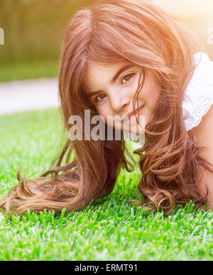Cute little girl lying down on fresh green grass field, having fun outdoors, relaxing on backyard, happy and carefree childhood Stock Photo