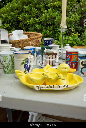 Collection of kitchen items for sale on a table at a garage sale.  Cute yellow duck egg cups set.  Second hand household items. Stock Photo