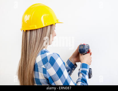 Young woman drilling a hole in the wall and wearing a protective helmet Stock Photo