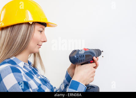 Young woman drilling a hole in the wall and wearing a protective helmet Stock Photo
