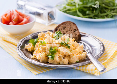 Scrambled eggs with fresh parsley on vintage metal plate, rye bread and tomato, selective focus Stock Photo