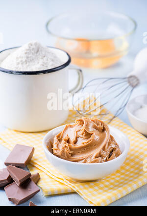 Peanut butter, chocolate chunks, eggs, sugar and cup of flour. Ingredients for baking. Selective focus Stock Photo