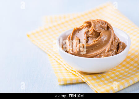 Creamy peanut butter in white bowl over yellow napkin, selective focus, copy space Stock Photo