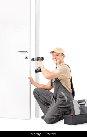 Vertical shot of a young locksmith screwing a lock on a door with a hand drill and looking at the camera Stock Photo