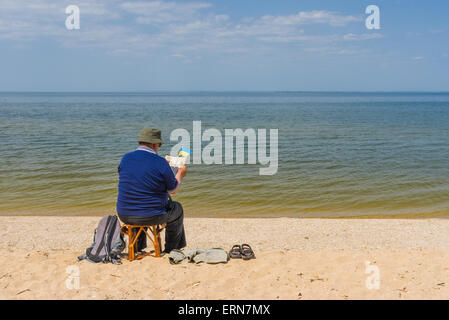Senior man reading book sitting on a beach of Dnepr river in Ukraine Stock Photo