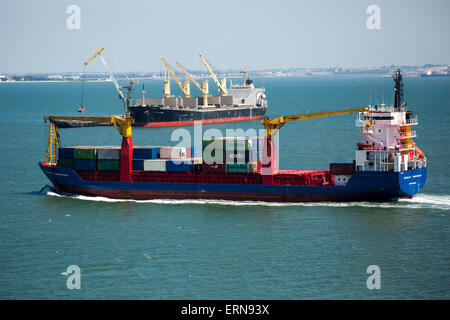 busy Lisbon harbour. Container ship heading for berth passing bulk carrier ship discharging cargo into barges. River Tagus. Stock Photo