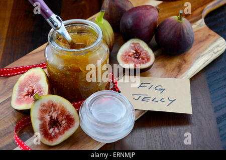 Fresh ripe Autumn fruit, figs, with fig jelly preserve in jar on cutting board against dark wood background. Stock Photo